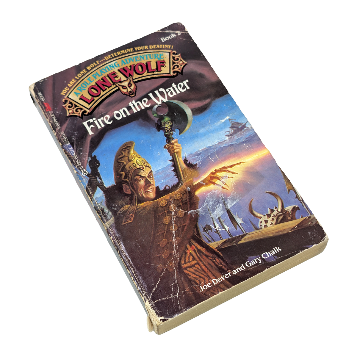A vintage paperback book of the Lone Wolf series, titled 'Fire on the Water', shown at an angle on a plain white background. The cover features a detailed fantasy illustration of a warrior holding a spear.