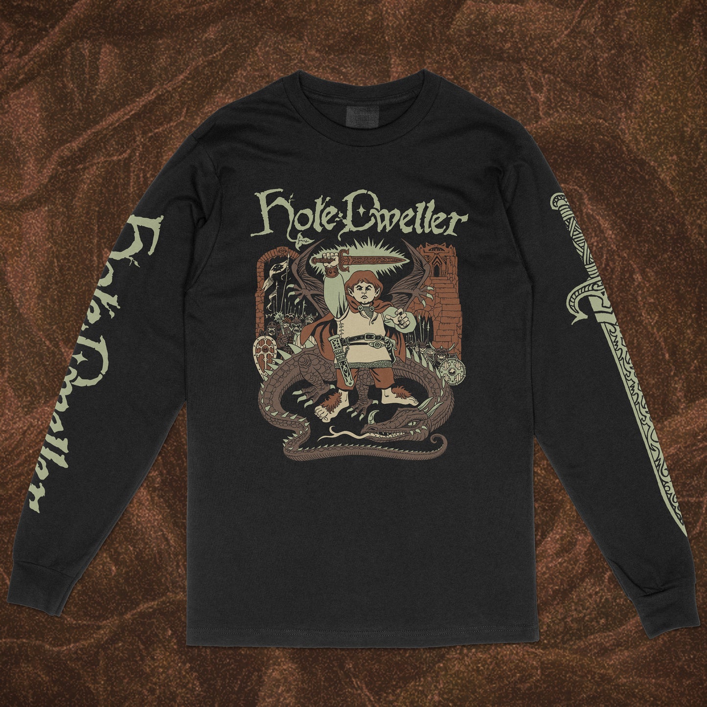 Black long-sleeve Comfort Colors shirt with 'Hole Dweller' graphic design featuring a hobbit holding a sword to the sky. The right sleeve reads Hole Dweller vertically, the left sleeve features a sword. The image is printed in tan, green and brown. The shirt is against a brown textured backdrop.
