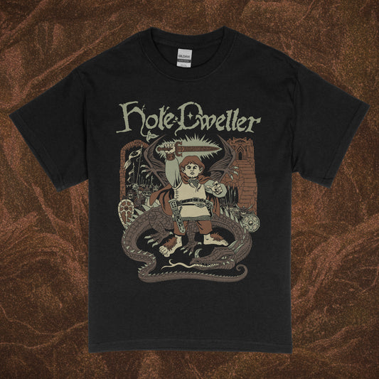 Black short-sleeve Gildan shirt with 'Hole Dweller' graphic design featuring a hobbit holding a sword to the sky. The right sleeve reads Hole Dweller vertically, the left sleeve features a sword. The image is printed in tan, green and brown. The shirt is against a brown textured backdrop.