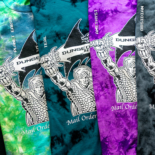 A earthy, teal, purple and black tie dye set of shirts featuring 'Mail Order Fantasy Music' text and illustrations screen printed on the front. The design depicts a man holding a sword with the words "Dungeons Deep Records" inscribed next to a fantasy dragon.