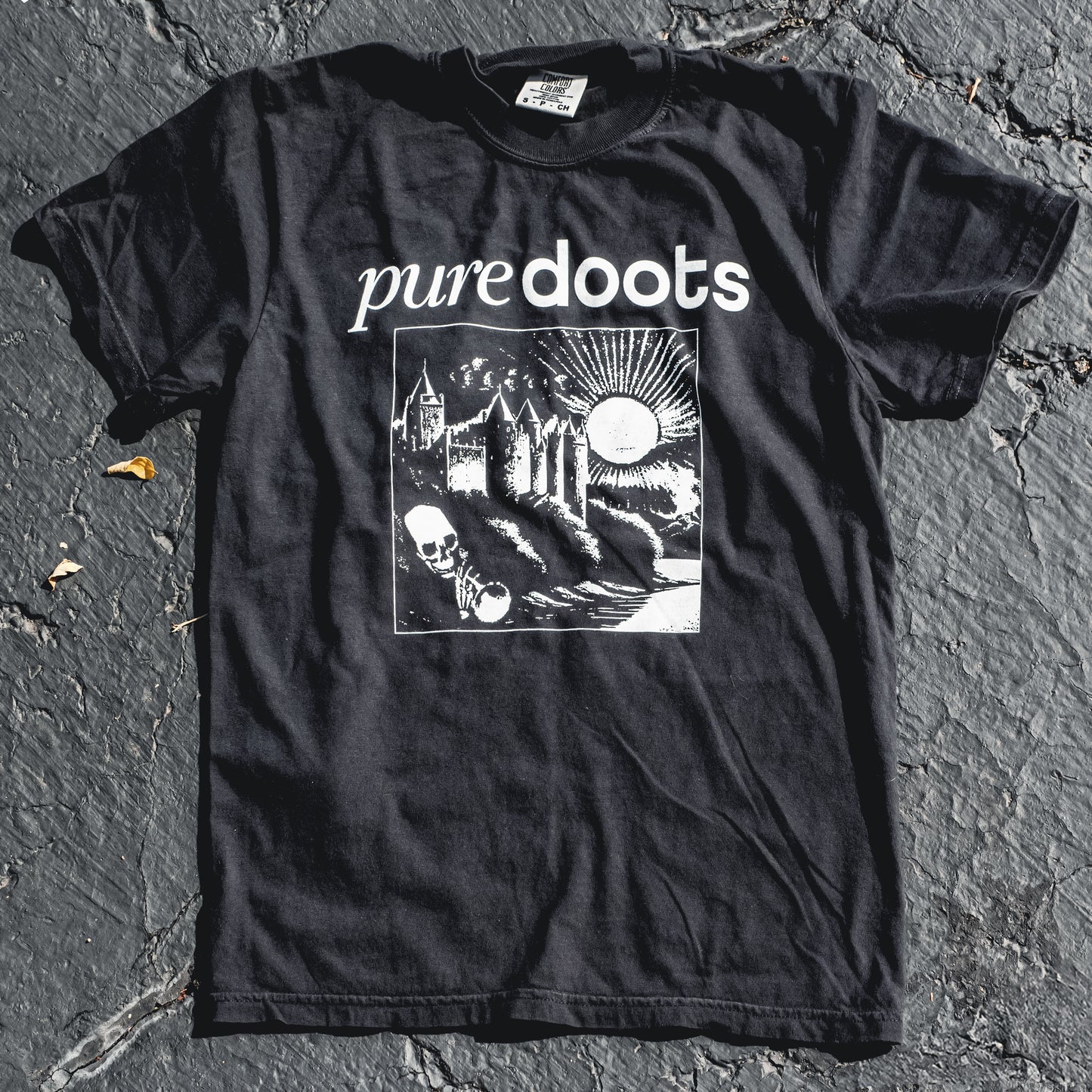 A black T-shirt with the text 'PUREDOOTS' and a screen printed design featuring a castle, moon, and skull on the front.