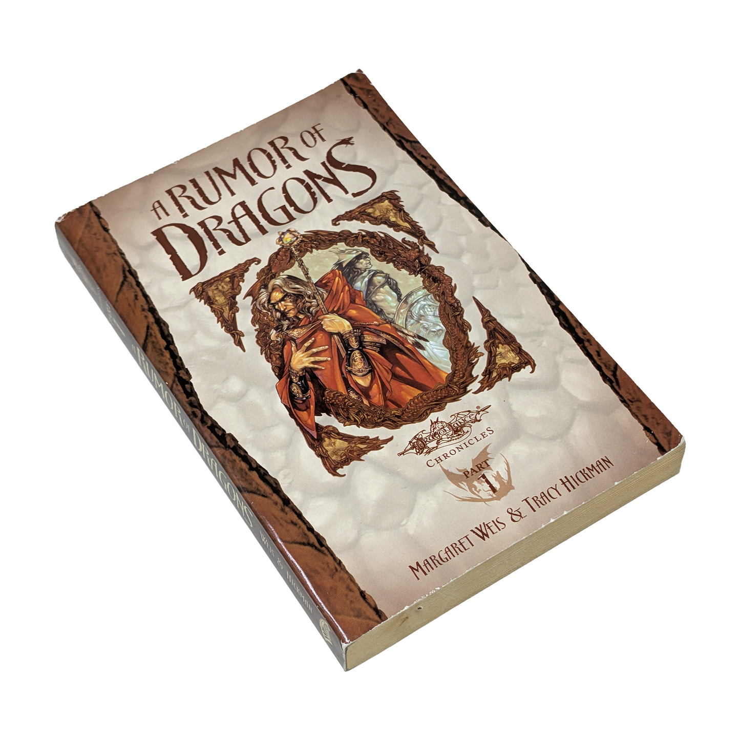 A boxed book or boxed set titled "A Rumor of Dragons" shown at an angle on a plain white background. The front cover features fantasy artwork with a robed figure in red and orange tones, and the spine/border appears brown with textured cream panels.