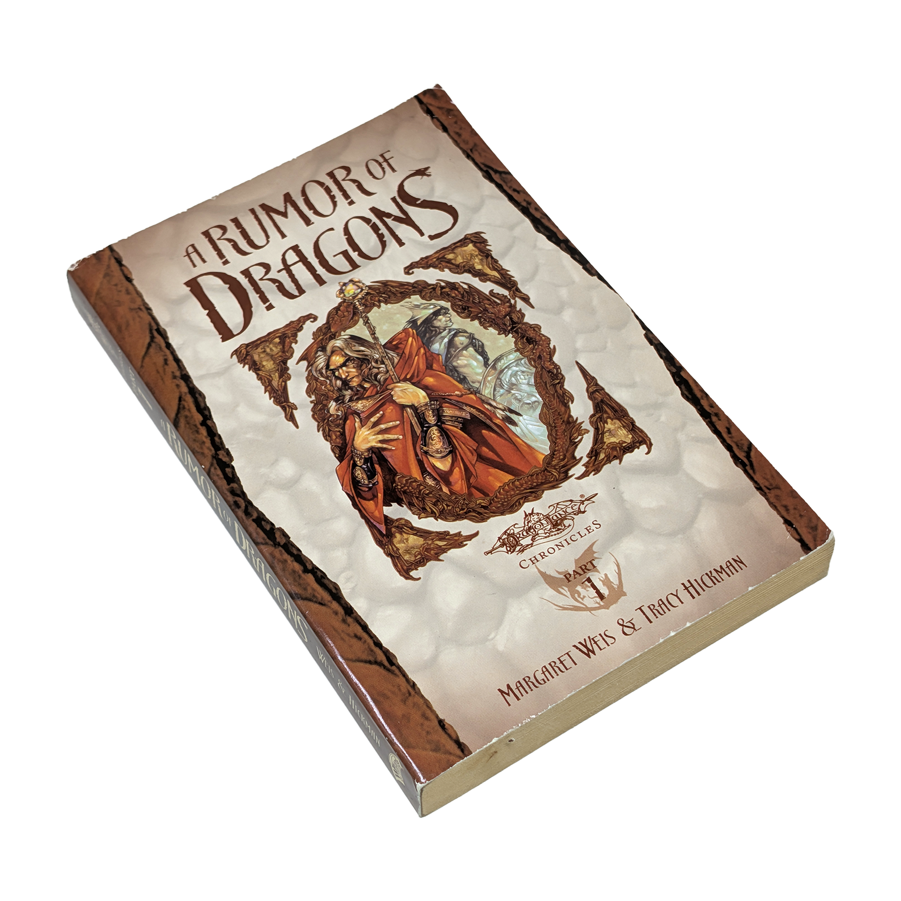 A boxed book or boxed set titled "A Rumor of Dragons" shown at an angle on a plain white background. The front cover features fantasy artwork with a robed figure in red and orange tones, and the spine/border appears brown with textured cream panels.