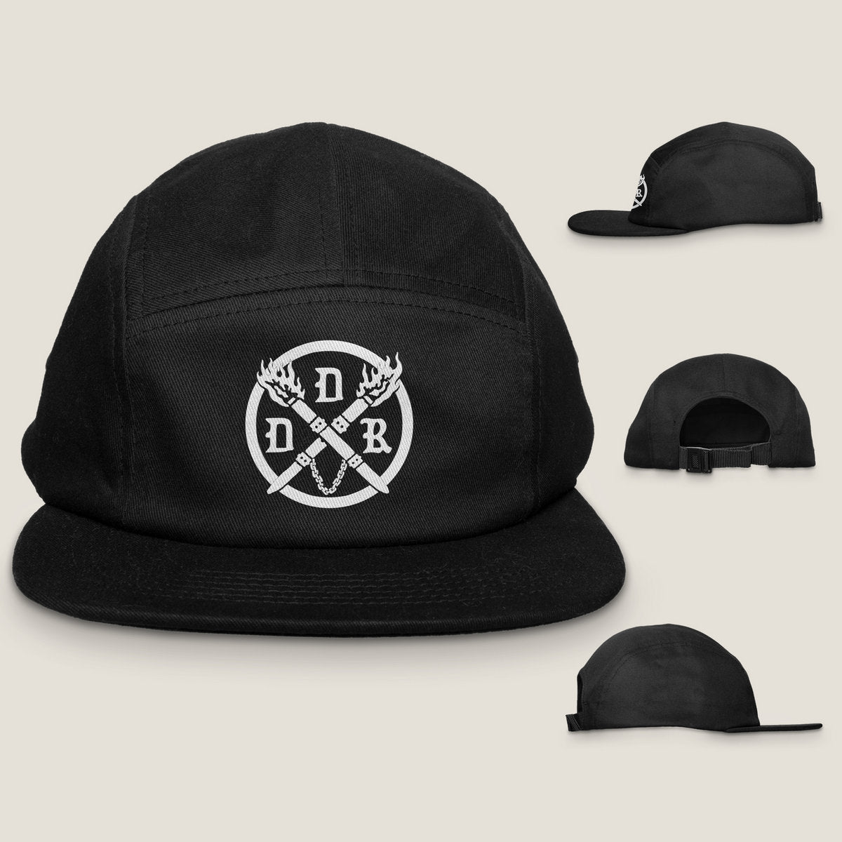 A black brushed cotton canvas camper style cap with a curved bill, featuring a white logo of crossed torches on the front. Shows front, back and side hat profiles.