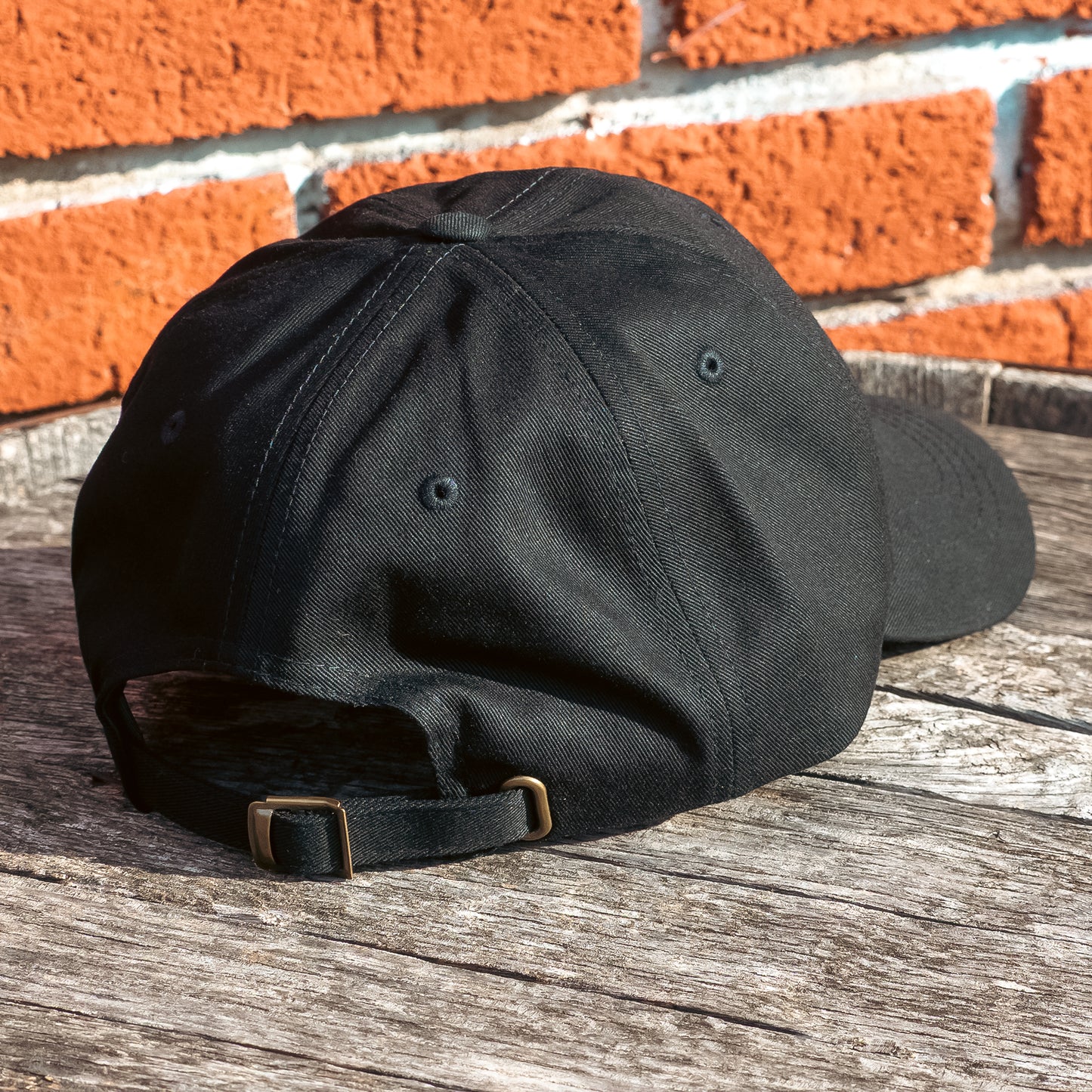 A black dad hat embellished with the Dungeons Deep Records "Mail Order Fantasy Music" Dragon emblem on a wooden backdrop.
