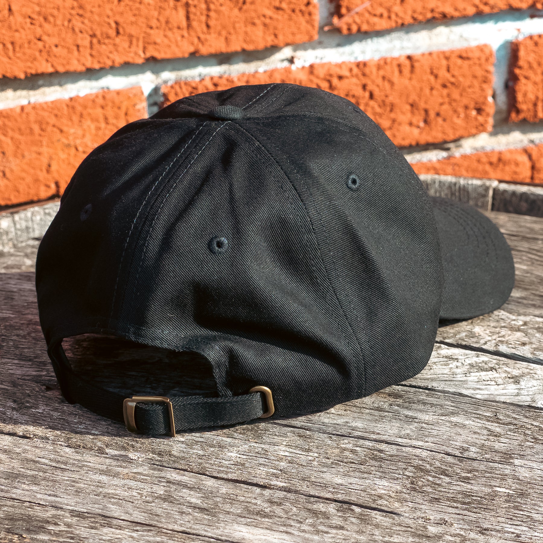 A black dad hat embellished with the Dungeons Deep Records "Mail Order Fantasy Music" Dragon emblem on a wooden backdrop.