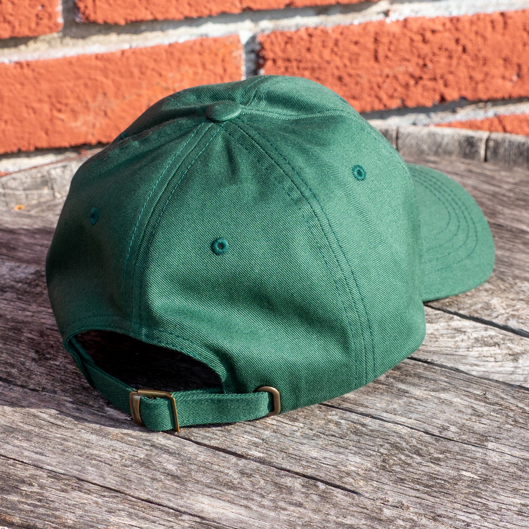 A green dad hat embellished with the Dungeons Deep Records "Mail Order Fantasy Music" Dragon emblem on a wooden backdrop.