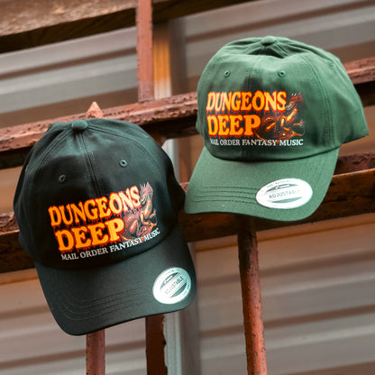 A black and green dad hat embellished with the Dungeons Deep Records "Mail Order Fantasy Music" Dragon emblem hanging from iron bars.