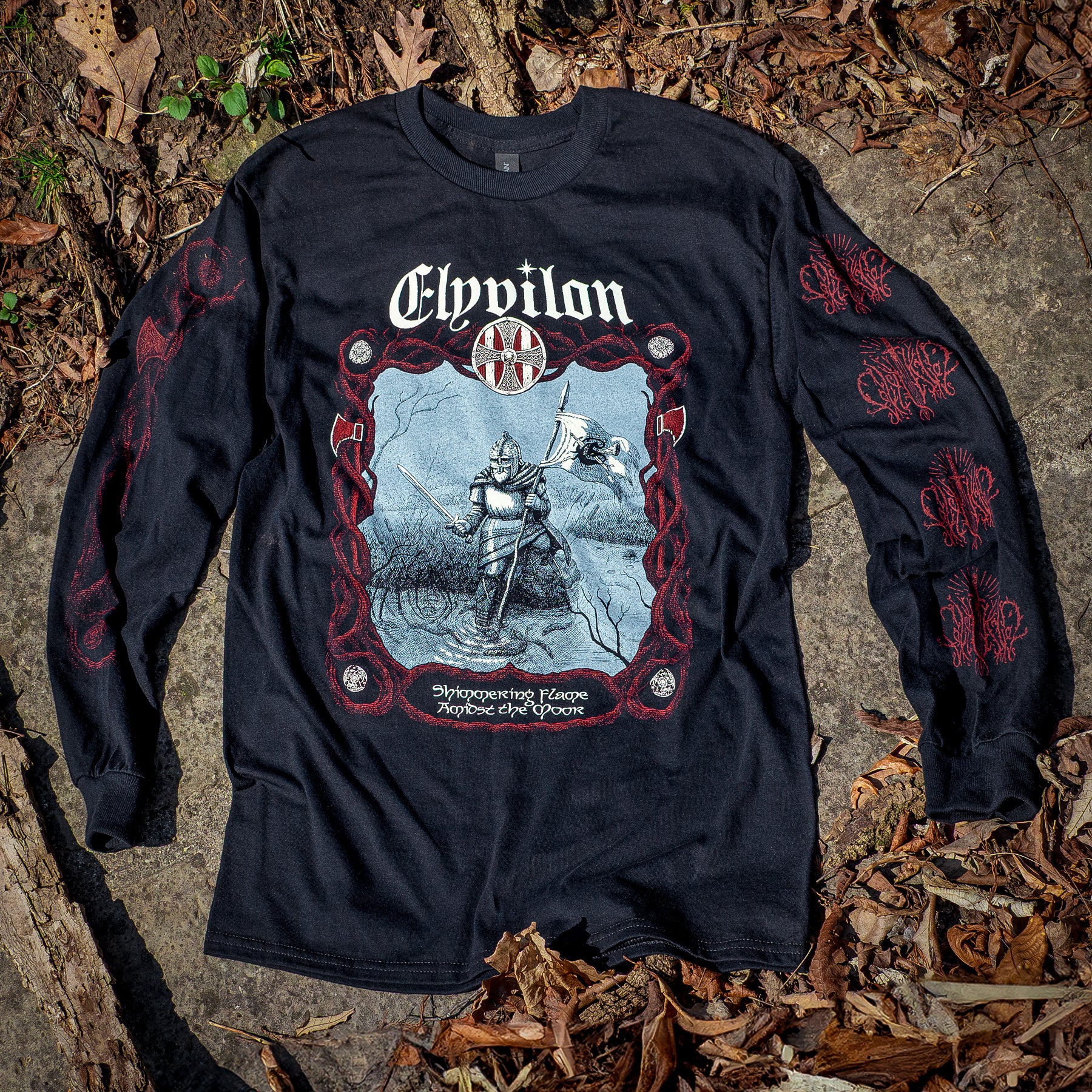 Black Long Sleeve T-Shirt. The left sleeve features the Elyvilon logo repeated four times in red ink spanning the length of the sleeve. The right sleeve features a red axe tangled in branches. The front shows a red, cream and blue image of a viking with the take Shimmering Flame Amidst the Moor. The Elyvilon arches over the top of the design.