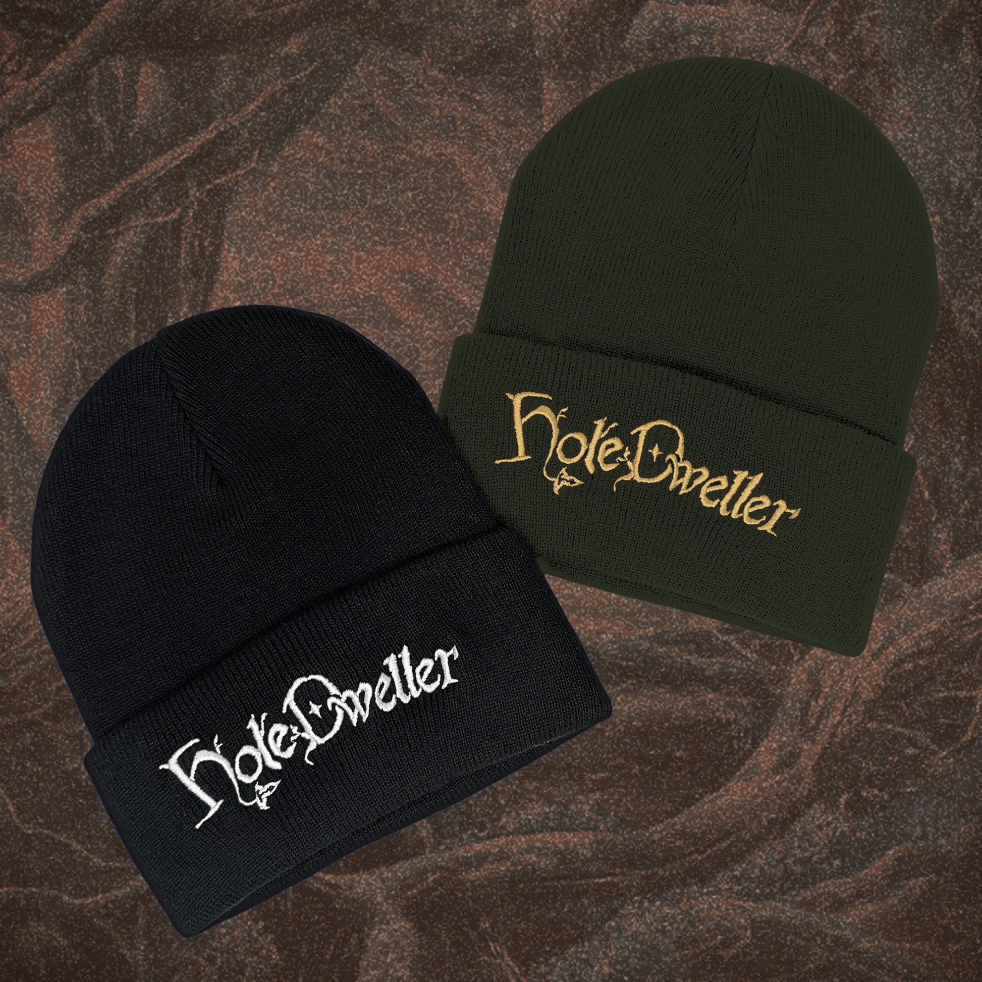 Two beanies, one black and one green, with 'Hole Dweller' embroidery on a textured brown background.
