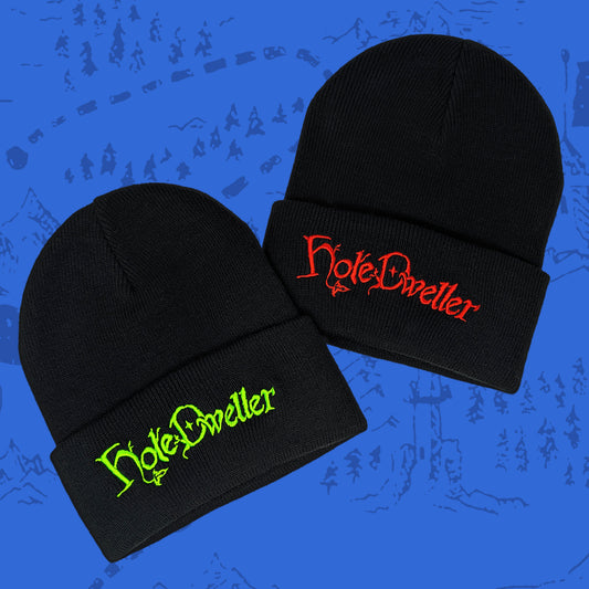 Two black beanies with 'Hole Dweller' text in red and green on a blue background.