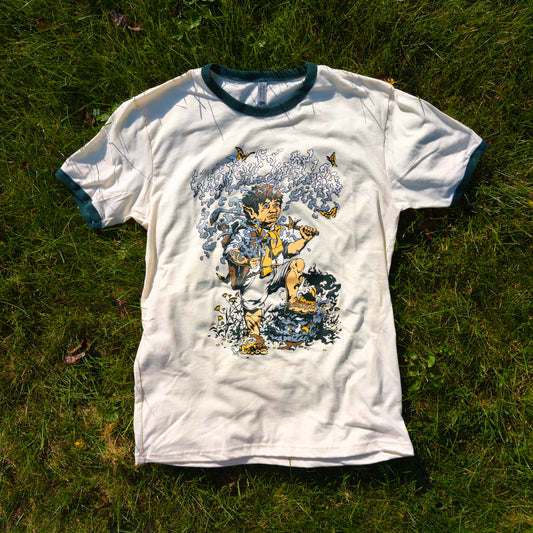 Natural cotton t-shirt with forest green ringers displaying a graphic of a hobbit holding a golf club with the title "Hole Dweller" above him which has formed from the smoke of the pipe the hobbit is holding. The shirt is resting on the grass.