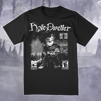 A black short-sleeve graphic t-shirt featuring a stylized print of the character Hyle Dweller with game-style rating logos, shown against a moody gray fantasy landscape background.