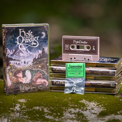 A themed setup featuring a 'Hole Dweller' cassette tape, a matching cassette cover, several stacked cassette cases, and a small clear bag of Jamwine  pewter miniature placed on a mossy surface with a blurred outdoor background.