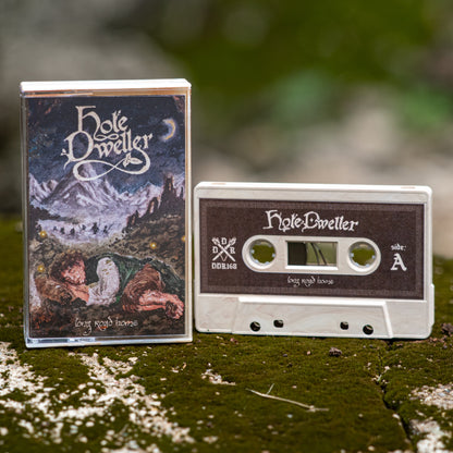 A cassette tape and its matching jewel case for the band Hole Dweller, titled 'Long Road Home', displayed on a mossy log with a blurred natural forest background.