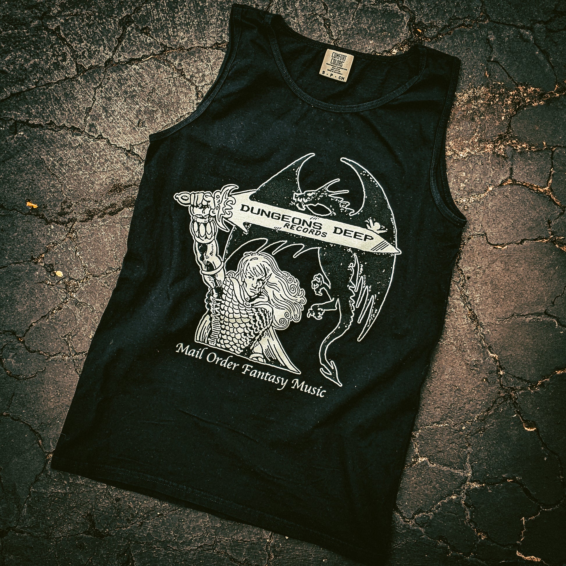 Black Comfort Colors tank top with 'Mail Order Fantasy Music' text and illustrations screen printed on the front. The design depicts a man holding a sword with the words "Dungeons Deep Records" inscribed next to a fantasy dragon.