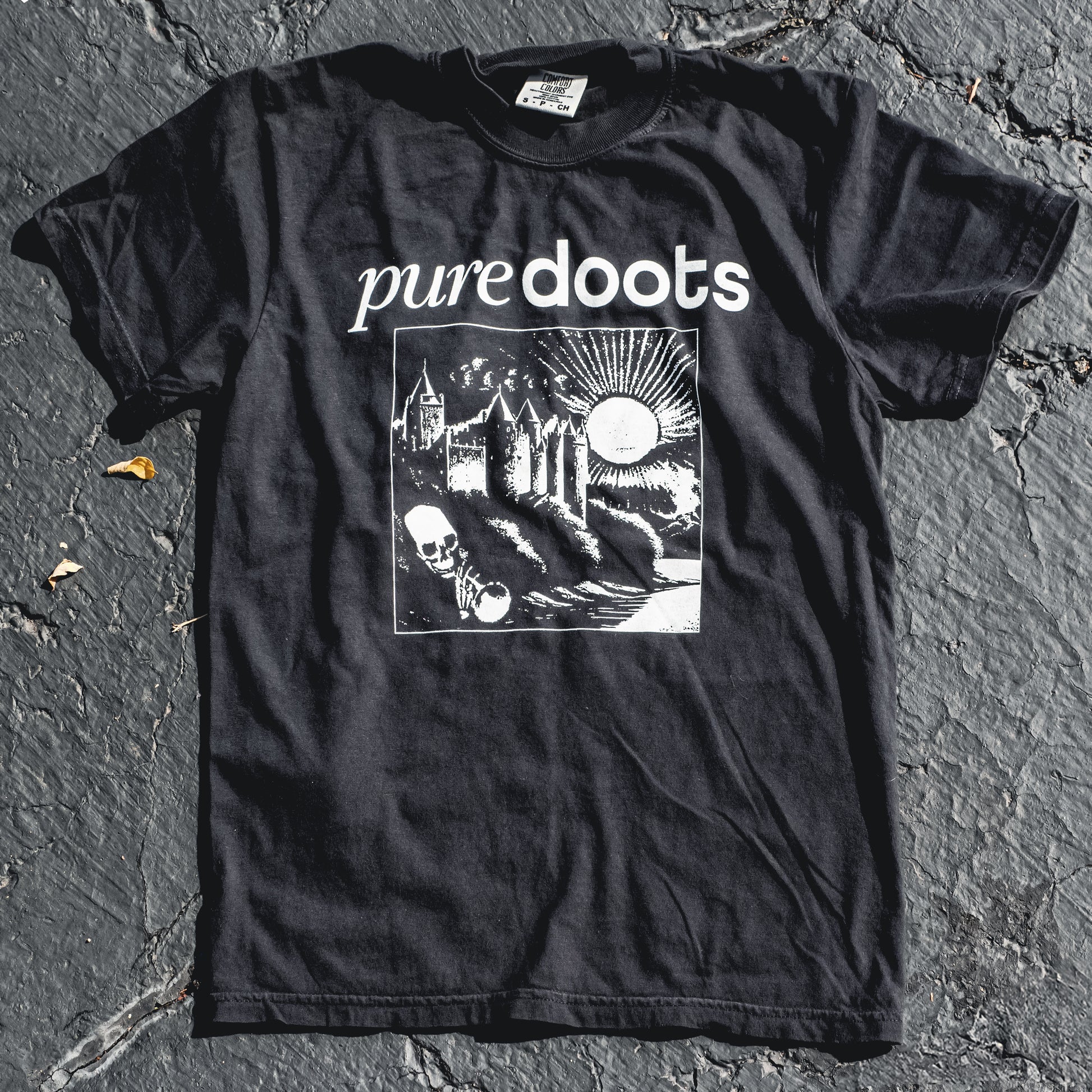A black T-shirt with the text 'PUREDOOTS' and a screen printed design featuring a castle, moon, and skull on the front.